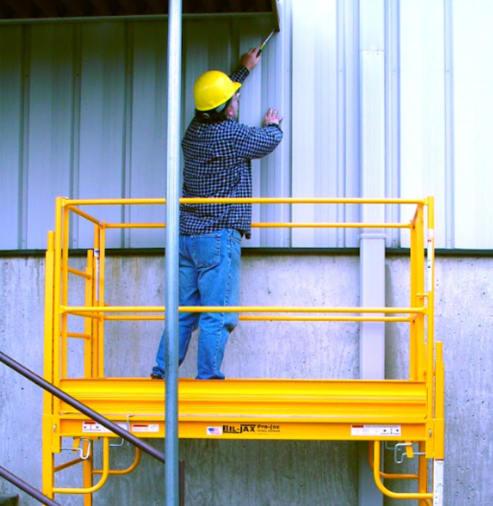 Worker standing on industrial scaffolding while installing metal wall panels.